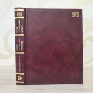 May include: A hardcover dictionary with a burgundy cover and spine. The spine features gold lettering and the title "Modern English-Russian Dictionary" and "New English-Russian Dictionary". The book is closed and standing upright.