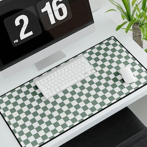 Op de afbeelding: Een groene en witte geruite bureaumat met een zwarte rand. Een wit toetsenbord en een witte muis liggen op de mat. Een computermonitor met een digitale klok die "2:16 PM" weergeeft, staat op de achtergrond.