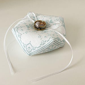 Peut inclure: Un coussin d'alliance brodé blanc et bleu avec un ruban de satin blanc et deux alliances dorées.