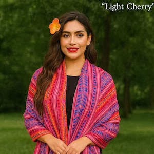 May include: A rectangular shawl featuring a vibrant pattern of vertical stripes in shades of pink, magenta, and blue with orange accents. The fabric has a textured weave and is finished with long, multi-colored fringe along the bottom edge.
