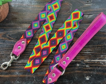 May include: A pink leather dog leash with a colorful woven strap. The strap features a rainbow of colors and a geometric diamond pattern.