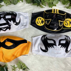 K&ouml;nnte beinhalten: Vier Wrestling-Masken, jede mit einem einzigartigen Design. Die Masken sind schwarz, wei&szlig; und gelb mit schwarzen und goldenen Akzenten. Die Masken sind aus Stoff und haben eine gl&auml;nzende Oberfl&auml;che. Die Masken sind mit den Namen "Ram 1", "Septiembre Negro", "El Solitario" und "Universo 2000" beschriftet.