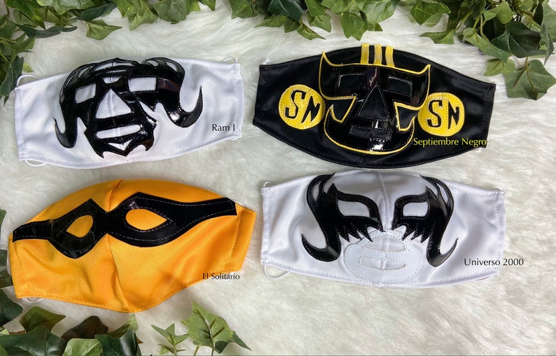 K&ouml;nnte beinhalten: Vier Wrestling-Masken, jede mit einem einzigartigen Design. Die Masken sind schwarz, wei&szlig; und gelb mit schwarzen und goldenen Akzenten. Die Masken sind aus Stoff und haben eine gl&auml;nzende Oberfl&auml;che. Die Masken sind mit den Namen "Ram 1", "Septiembre Negro", "El Solitario" und "Universo 2000" beschriftet.
