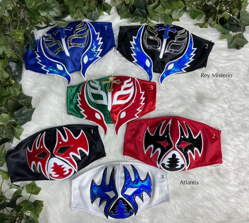K&ouml;nnte beinhalten: Sechs Wrestling-Masken, jede mit einem einzigartigen Design und Farbschema. Die Masken sind aus Stoff und haben eine Vielzahl von Verzierungen, darunter Glitzer, Pailletten und Stickereien. Die Masken sind mit Nummern und Namen gekennzeichnet, darunter "Rey Mysterio" und "Atlantis".