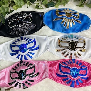 K&ouml;nnte beinhalten: Sechs Luchador-Masken in verschiedenen Farben. Die Masken sind aus Stoff und haben ein goldenes, blaues oder schwarzes Design. Die Masken sind von 1 bis 6 nummeriert.