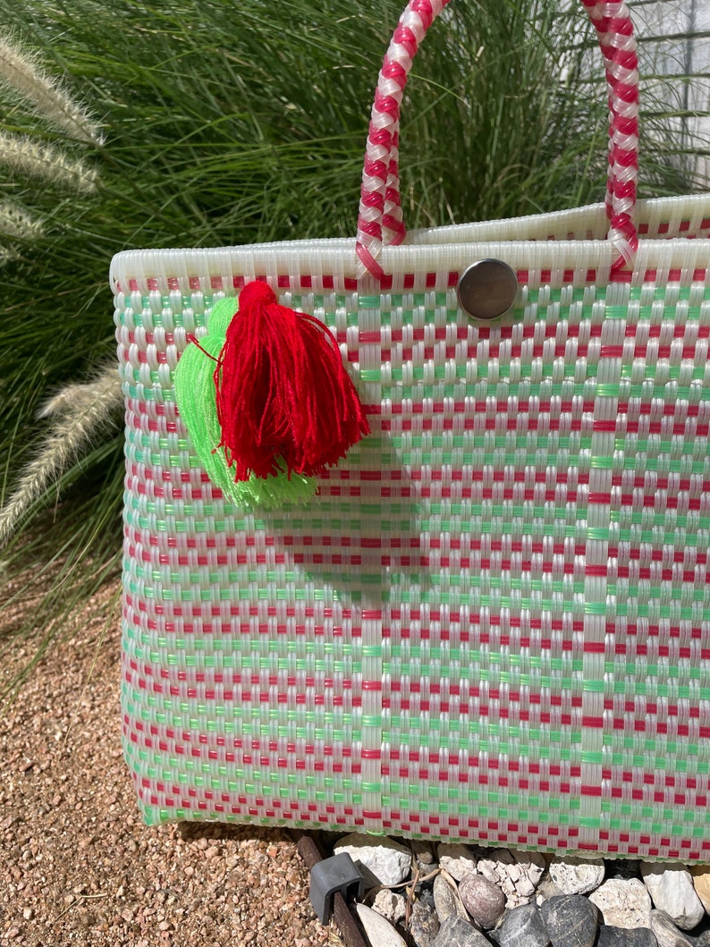 May include: A white woven tote bag with red and green stripes. The bag has a red and green handle and a red tassel.