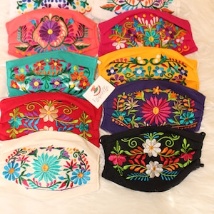 Pode incluir: Uma coleção de dez máscaras faciais coloridas com bordados florais. As máscaras são feitas de tecido de algodão e têm uma variedade de cores, incluindo vermelho, rosa, amarelo, verde, azul e roxo. O bordado é intrincado e detalhado, com flores, folhas e outros motivos florais.