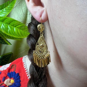 Peut inclure: Boucles d'oreilles pendantes en or avec un motif de filigrane et une frange de petites barres dorées.