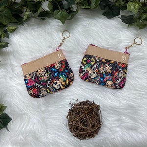 May include: Two small, colorful coin purses with a patterned design featuring skulls and floral elements. Each purse has a tan leather top and a gold keychain. The purses are labeled with the numbers 9 and 10.