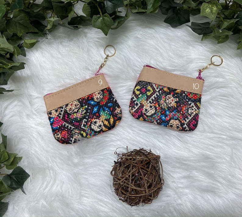 May include: Two small, colorful coin purses with a patterned design featuring skulls and floral elements. Each purse has a tan leather top and a gold keychain. The purses are labeled with the numbers 9 and 10.