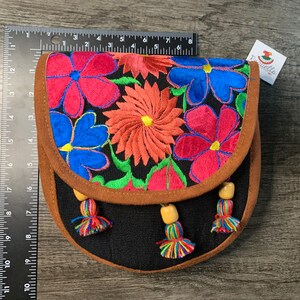 May include: A black fabric purse with a brown suede flap and colorful embroidered flowers. The purse has a beaded tassel on each side.