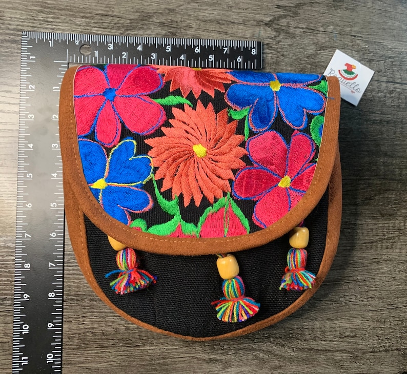 May include: A black fabric purse with a brown suede flap and colorful embroidered flowers. The purse has a beaded tassel on each side.