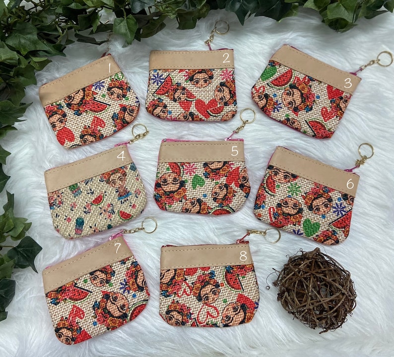 May include: Eight small, square coin purses with a Frida Kahlo design. The purses have a beige top and a zipper closure. The main body of the purses features a burlap-like fabric with a colorful Frida Kahlo print, including watermelons and flowers.