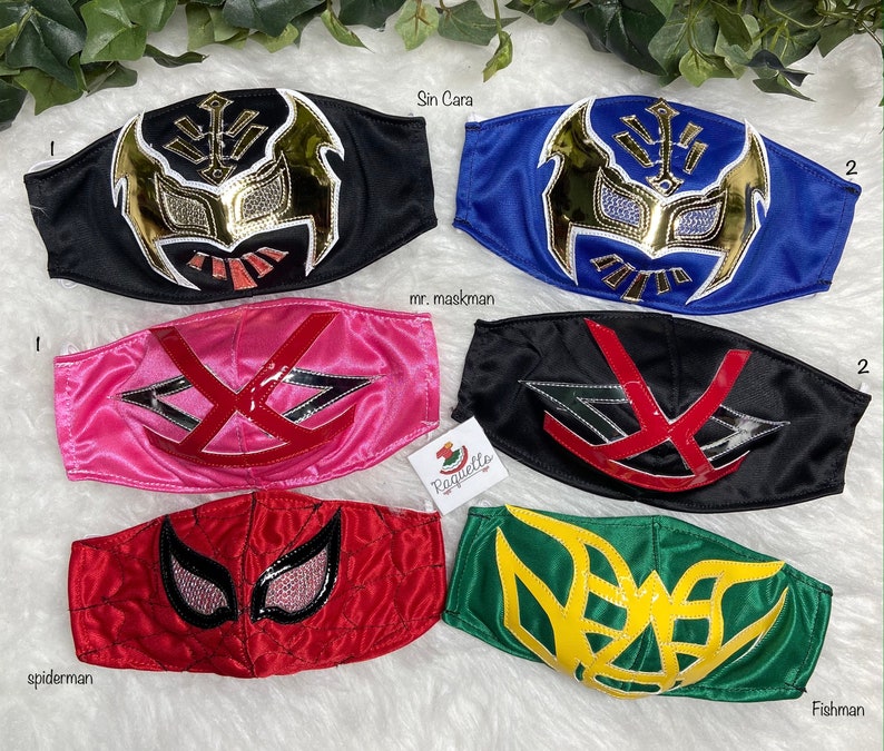 K&ouml;nnte beinhalten: Sechs bunte Stoffmasken mit verschiedenen Wrestling-Charakterdesigns. Die Masken sind schwarz, blau, rosa, rot, gr&uuml;n und gelb. Die Masken haben verschiedene Designs, darunter einen Sch&auml;del, eine Spinne und einen Fisch.