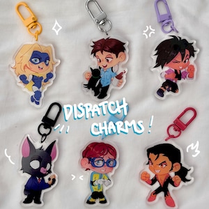 May include: A selection of acrylic charms with cartoon character designs in various colours. Each charm depicts a different character in a unique pose, attached to keychains with different coloured clasps. The text "DISPATCH CHARMS!" is visible in a turquoise font.