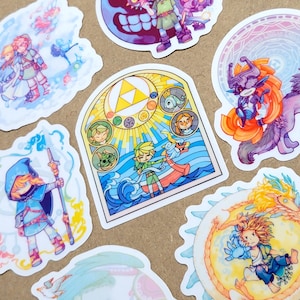 May include: A collection of colorful stickers featuring characters and scenes from a video game. The stickers showcase various designs, including a stained-glass style image, a character with a mask, and other fantasy-themed illustrations. The stickers are on a light brown surface.