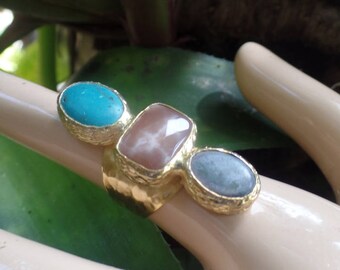 May include: Gold ring with three gemstone settings. The stones are turquoise, pink, and green.