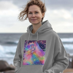 Puede incluir: Una sudadera con capucha gris con un gráfico colorido y abstracto en la parte delantera. El gráfico es una mezcla de colores arcoíris y formas. La sudadera tiene una capucha con cordón y un bolsillo delantero. El fondo es una imagen borrosa del mar.