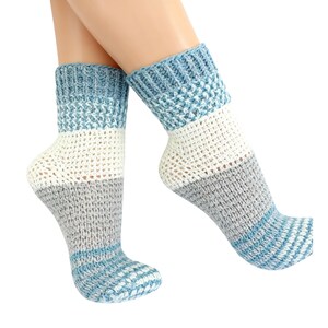 Peut inclure: Une paire de chaussettes tricotées à la main, multicolores. Les chaussettes présentent un revers bleu, une section blanche et une section grise. Les orteils et les talons sont bleus avec un motif rayé. Les chaussettes sont en matière tricotée.