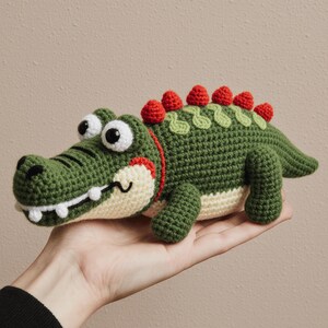 Peut inclure: Un jouet en crochet fait à la main représentant un alligator vert avec des dents blanches, de grands yeux globuleux et des accents rouges. L'alligator a une épine dorsale rouge et verte. Un animal en peluche amusant et fantaisiste.