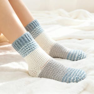 Peut inclure: Paire de chaussettes tricotées avec un motif de blocs de couleurs bleu, blanc et gris. Les chaussettes ont une bordure côtelée et un motif de tricot texturé. Les chaussettes sont présentées sur une surface blanche.