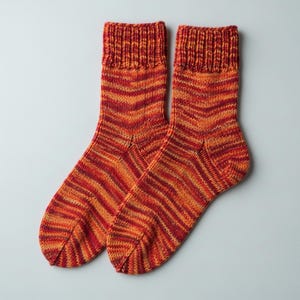 Peut inclure: Une paire de chaussettes tricotées à la main, aux couleurs rouge, orange et jaune. Les chaussettes présentent un bord-côte et un motif rayé sur toute la longueur. Fabriquées dans une matière douce et chaude, idéales pour l'hiver.