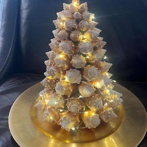 May include: A seashell Christmas tree decorated with white fairy lights, sitting on a gold charger plate.