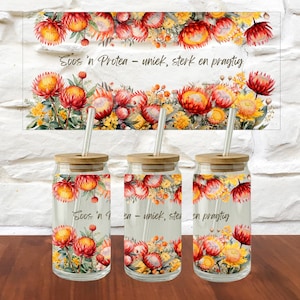 Puede incluir: Tres vasos de vidrio transparente con tapas de bambú y pajitas, con un estampado floral de flores protea rojas y amarillas y follaje verde. El texto "Soos 'n Protea – uniek, sterk en pragtig" está impreso en el vidrio en letra cursiva.