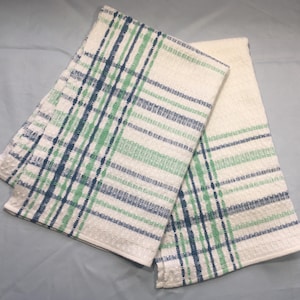 May include: Two white kitchen towels with a plaid pattern in shades of blue and green. The towels are folded and have a textured weave. The towels are suitable for kitchen use.