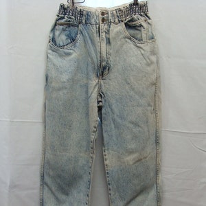 May include: Acid wash denim jeans with an elastic waistband and button closure. The light blue jeans have front and back pockets, and a tapered leg with a split hem detail. The jeans are hanging on a hanger.