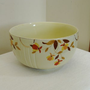 May include: A cream-colored ceramic bowl with a floral design in shades of red, yellow, and brown. The bowl has a gold rim and vertical ribbed detailing. The floral pattern is arranged in a repeating design around the bowl.