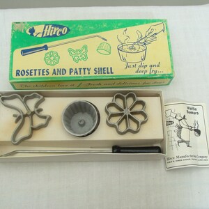 May include: Vintage Hirco Rosettes and Patty Shell set. The box is green and yellow with illustrations and text. The set includes metal rosette molds in various shapes, a patty shell mold, and a handle. A recipe booklet is included.
