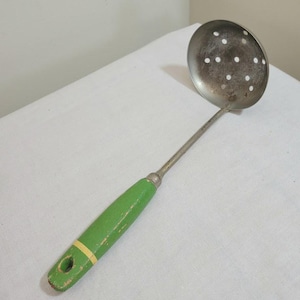 May include: Vintage metal skimmer with a round, perforated head and a long handle. The handle is painted green with a yellow stripe near the end. The skimmer is designed for straining liquids and removing solids.