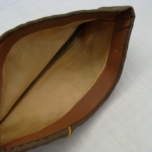 May include: An olive drab military garrison cap with a tan interior and a brown leatherette trim. The cap has a simple, folded design and a small yellow accent near the brim. The interior fabric shows signs of wear.