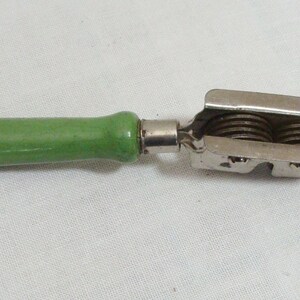 May include: A vintage kitchen tool with a green wooden handle and a metal cutting head. The cutting head features two circular blades. The tool is designed for a specific food preparation task, likely slicing or cutting.