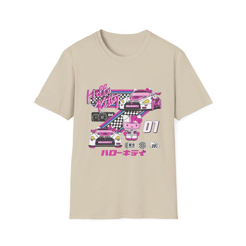 Op de afbeelding: Een beige T-shirt met een Hello Kitty race-thema. Het ontwerp toont Hello Kitty in een roze racepak, rijdend in een witte raceauto met roze accenten. De tekst "Hello Kitty" is in roze en wit, en de tekst "ハローキティ" is in roze.