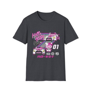 Op de afbeelding: Een donkergrijs T-shirt met een Hello Kitty race-thema. Het shirt heeft een roze Hello Kitty-personage in een racepak, twee roze en witte raceauto's en de tekst "Hello Kitty" en "ハローキティ".