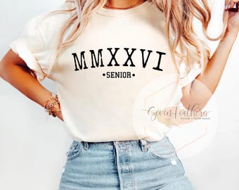 May include: Cream-colored t-shirt with the text "MMXXVI • SENIOR" in black. The shirt is paired with blue jeans. The image also includes a logo for "Seven Feathers Boutique & Custom Apparel".