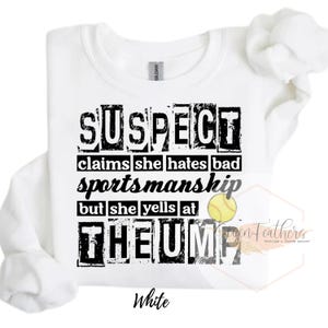 Puede incluir: Camiseta blanca con texto negro que dice "SUSPECT claims she hates bad sportsmanship but she yells at THEUMP". Una pelota de softball amarilla es visible en el texto.