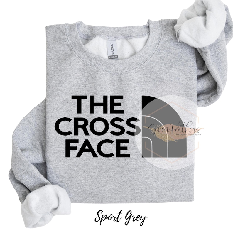 Pu&ograve; includere: Una felpa grigia con il testo "THE CROSS FACE" in lettere nere. Il testo &egrave; stilizzato per assomigliare al logo di The North Face. La felpa &egrave; disponibile in Grigio Sport.