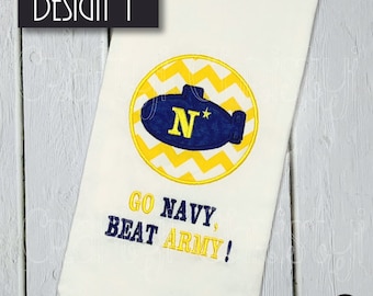 Può includere: Un asciugamano da cucina bianco con un cerchio a motivo chevron giallo e bianco che rappresenta un sottomarino blu con una stella bianca e la lettera N all'interno. Il testo "GO NAVY, BEAT ARMY!" si trova sotto il cerchio.
