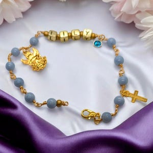 May include: A blue and gold beaded bracelet with a gold angel charm, a gold cross charm, and a gold charm with the name "Lily" spelled out.