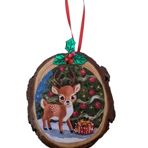 May include: A round, wooden Christmas ornament featuring a hand-painted scene of a deer standing in front of a Christmas tree with red ornaments and a wrapped gift. The ornament has a red ribbon for hanging and is decorated with green holly.