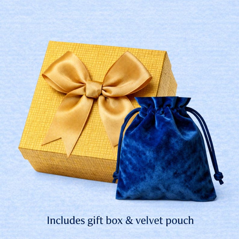May include: A gold gift box with a matching satin bow and a blue velvet drawstring pouch. The gift box has a textured surface. The text at the bottom reads, "Includes gift box & velvet pouch."
