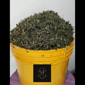 May include: A bright yellow plastic bucket filled to the brim with dried, dark green leafy herbs. A black square label is centred on the front of the bucket, featuring the gold letters SF surrounded by a delicate, circular botanical wreath design.