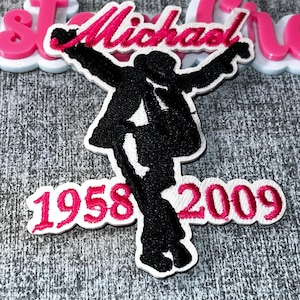 May include: A black and white embroidered patch featuring a silhouette of a person in a dance pose. The name "Michael" is embroidered in pink, along with the years "1958 2009". Additional pink text is visible.