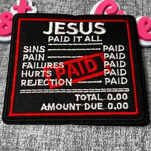 May include: Black and red embroidered patch with the text "JESUS PAID IT ALL." The patch lists "SINS, PAIN, FAILURES, HURTS, REJECTION" with "PAID" next to each. A red "PAID" stamp is across the center.