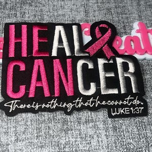 Puede incluir: Un parche bordado negro con el texto HEAL CANCER en hilo rosa y blanco, con un lazo de concienciación rosa que reemplaza la letra A. Debajo, el texto dice There is nothing that he cannot do. LUKE 1:37 en letra cursiva blanca.