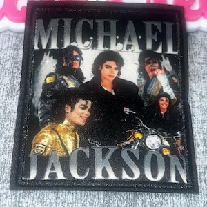 May include: Black rectangular patch featuring multiple images of Michael Jackson with the name "MICHAEL JACKSON" in silver lettering. The patch has a black border and a textured surface.