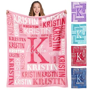 May include: A pink fleece blanket featuring the name "Kristin" in a repeating pattern. A large pink "K" and the name "Kristin" are central. Additional blankets in purple, blue, red, and navy are also shown. The blanket is designed for comfort.
